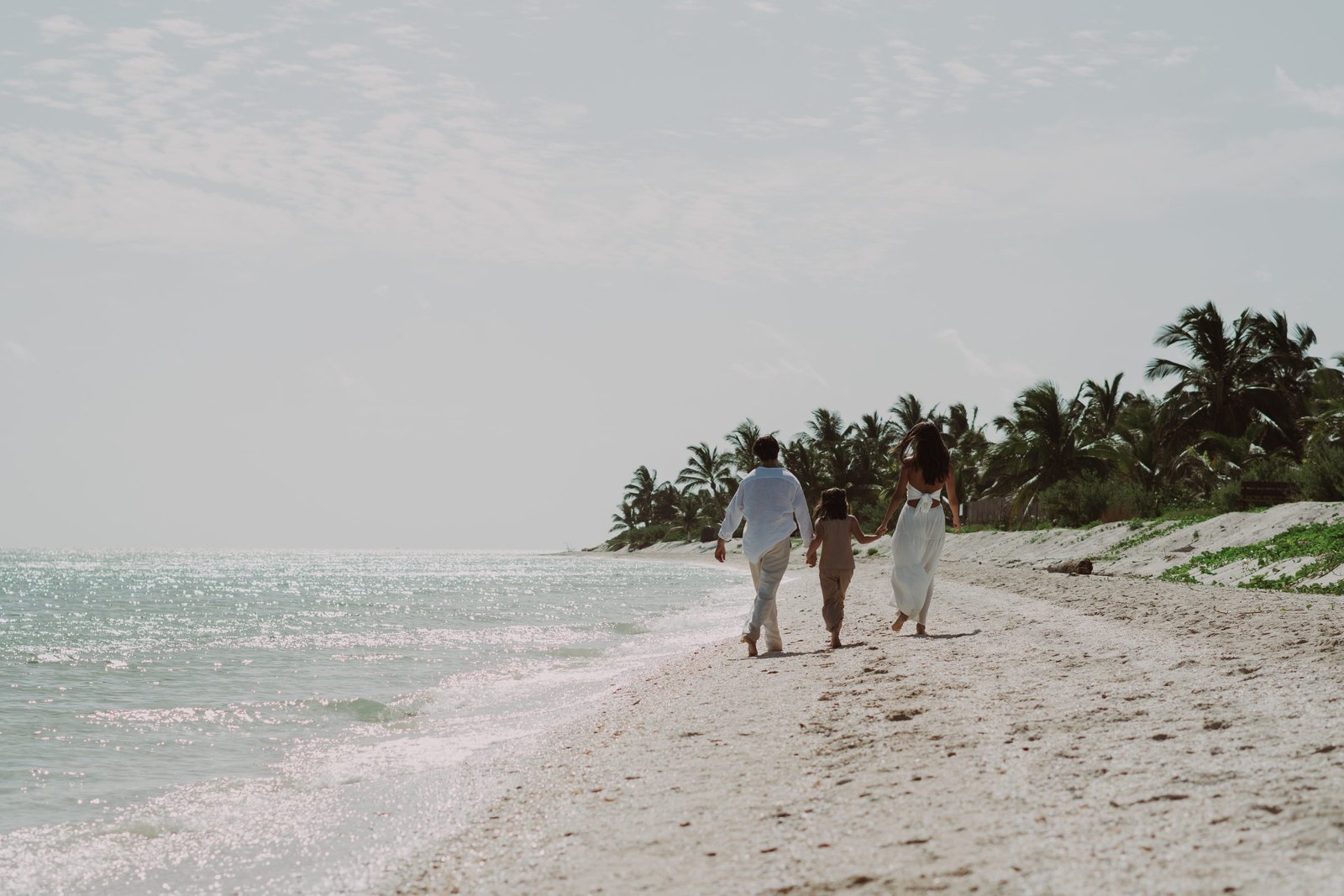 Familia caminando junta por la playa hacia las palmeras